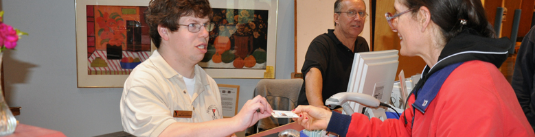 Young man working behind the counter at the YMCA, handing a membership card to a smiling  gym member